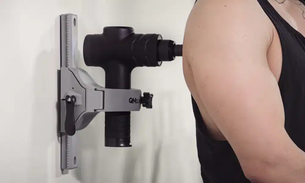 Man getting a deep hands free Massage using Massage Gun Holder Wall Mount mounted permanently via screws to wall Works with many Massage and Percussion Guns like Theragun and others